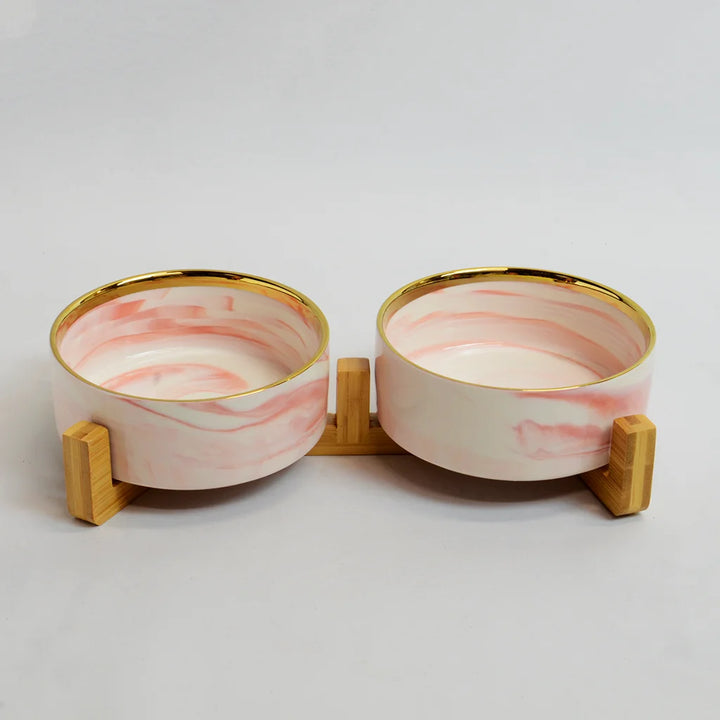 Two pink marble-look bowls with gold rims on a raised bamboo stand